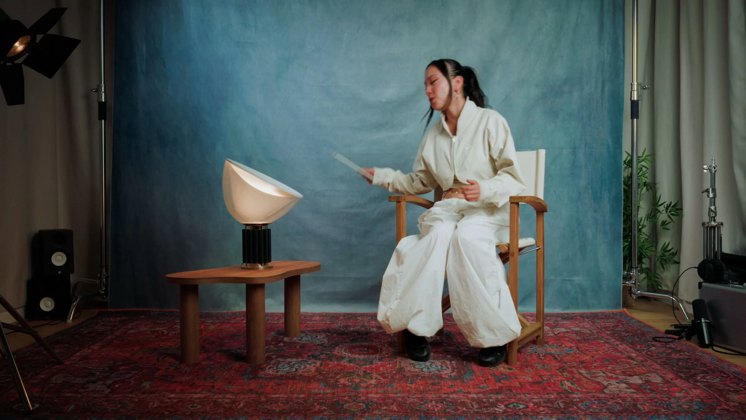 Le plateau de DOGMA : Filiz assise dans un fauteuil, tablette en main, devant une toile bleue, une lampe et un tapis rouge